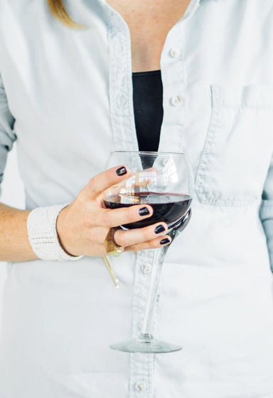 Off center red wine glass, held in a woman's hand 