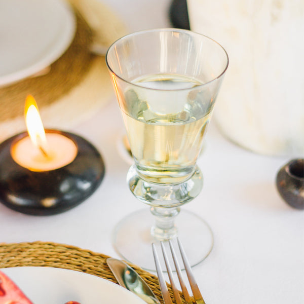 White wine in an olive green tinted wine glass with a decorative stem. 