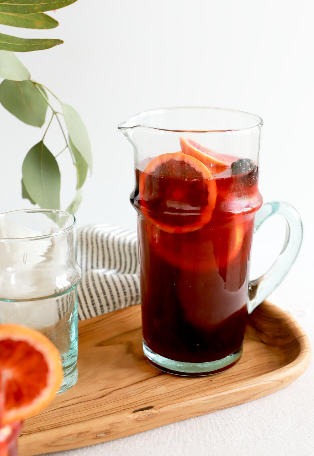 Moroccan recycled glass pitcher with curves and a handle. Styled with sangria at a dinner party. 